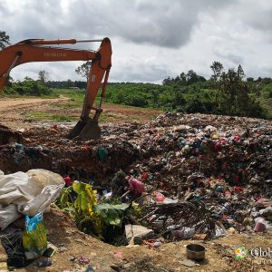 Scavengers working in the rubbish pit near heavy machinery.