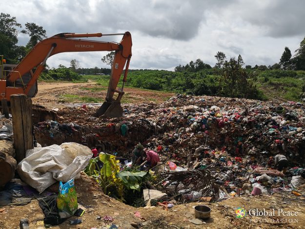 Scavengers working in the rubbish pit near heavy machinery.